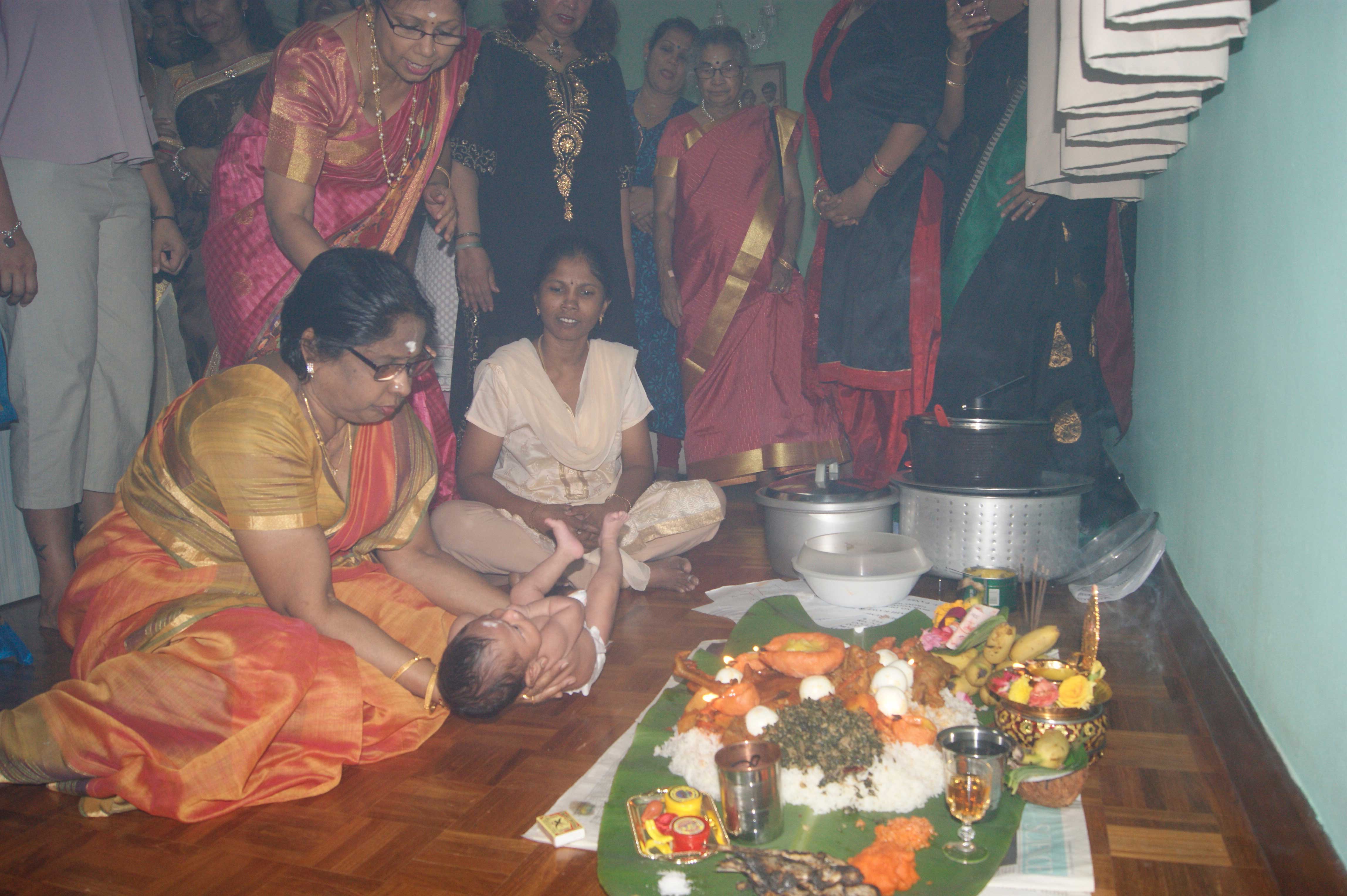Madam Rajeshwari Govindasamy holding the baby in front of the <i>padayal</i> or food offering for Sri Periyachi Amman, a deity believed to be the protector of infants. This prayer ceremony is attended by only women and is held when the child is either 16 days or 30 days old.